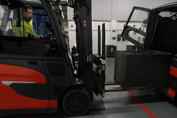 forklift operator in a bright yellow vest maneuvers a forklift, lifting a black container in Texas