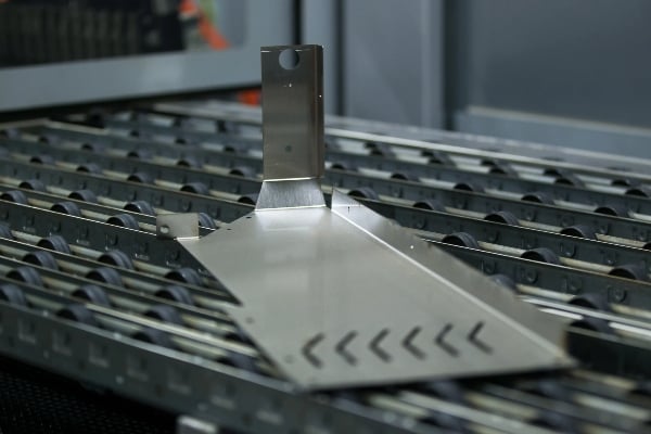 The metal plate is being processed on a conveyor belt with rollers in a manufacturing factory in Texas